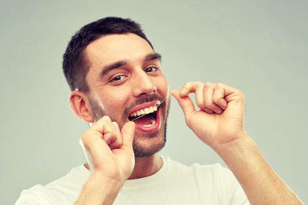 assistenza sanitaria, igiene dentale, persone e concetto di bellezza - giovane sorridente con il filo interdentale che pulisce i denti su sfondo grigio