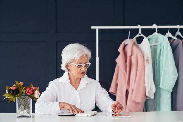 Assistenza stile moda. Stile di vita aziendale senior. Donna anziana sicura sul tablet di navigazione sul posto di lavoro.