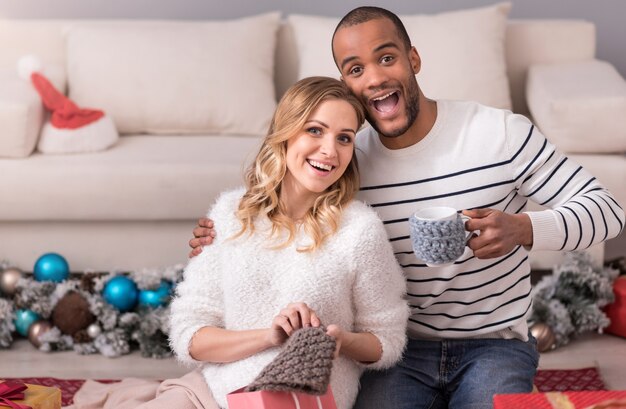 Assolutamente felice. Giovani coppie positive allegre che si siedono e che sorridono mentre tengono i loro regali di Natale