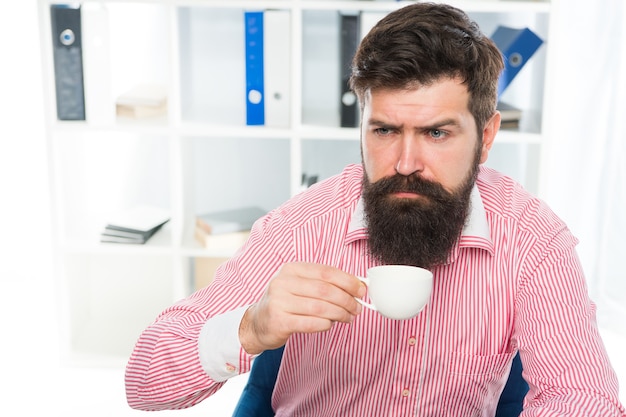 Assonnato mezzo sveglio hipster bere una tazza di caffè sul posto di lavoro, caffeina.