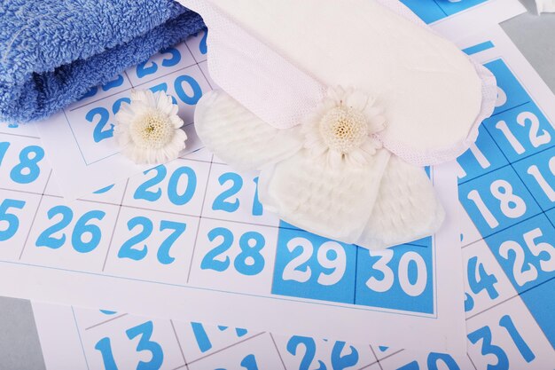 Assorbenti igienici fiori bianchi e asciugamano su sfondo blu del calendario