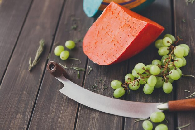 Assortimento del negozio di formaggi. Natura morta con pesto di gouda rosso e blu, uva bianca, erbe aromatiche e coltello a due mani. Copia spazio, sfondo