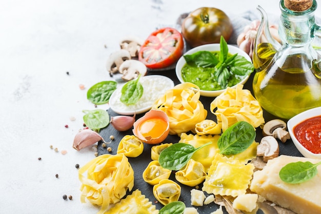 Assortimento di cibo italiano e ingredienti ravioli con ricotta e spinaci tortellini pesto salsa di pomodoro olio d'oliva parmigiano copia spazio sullo sfondo