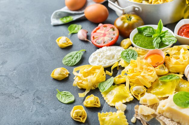 Assortimento di cibo italiano e ingredienti ravioli con ricotta e spinaci tortellini pesto salsa di pomodoro olio d'oliva parmigiano copia spazio sullo sfondo