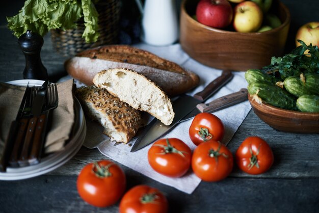 Assortimento di cibo vegetariano sul tavolo servito per colazione - pomodori freschi, cetrioli, mele, pane fatto in casa su tovagliolo di cotone e piatti