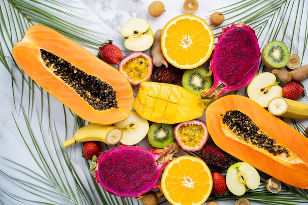 Assortimento di diversi frutti esotici con foglie tropicali su fondo di marmo bianco. Vista dall'alto, piatto. Alimentazione sana, dieta, frutta di stagione estiva.