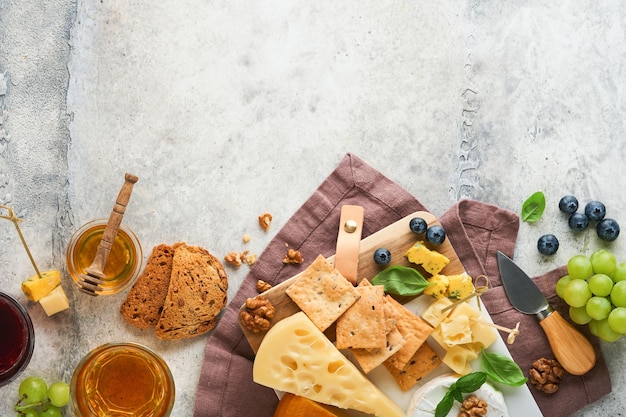 Assortimento di formaggio cracker miele mirtilli uva con vino rosso e bianco in bicchieri antipasto server su marmo bianco su sfondo grigio Spazio piatto per la copia