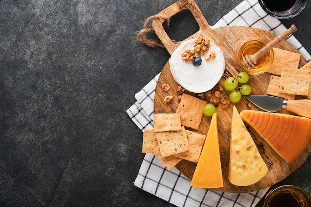 Assortimento di formaggio cracker miele mirtilli uva con vino rosso e bianco in bicchieri antipasto server su tavola di marmo bianco su vecchio sfondo grigio scuro Spazio piatto per la copia