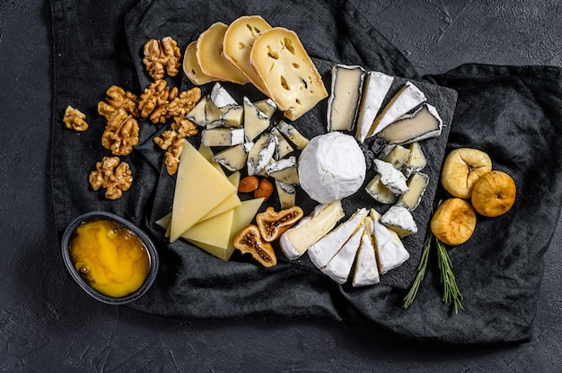 Assortimento di formaggio francese con miele, noci e fichi sul tagliere. Antipasto italiano. Sfondo nero. Vista dall'alto