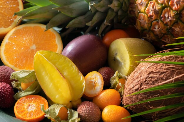 Assortimento di frutta esotica tropicale: metà di arance, litchi, carambole, ananas, limone, physalis, cocco, litchi con foglie di palma da vicino