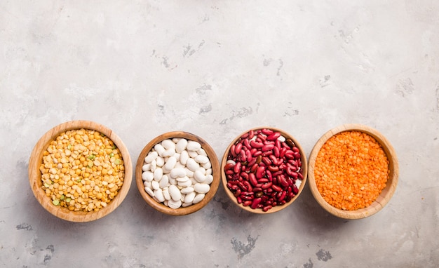 Assortimento di lenticchie, ceci e fagioli in diverse ciotole sul tavolo di pietra bianca.