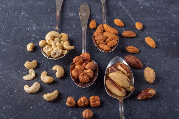 Assortimento di noci di acagiù, nocciole, mandorle, noci del Brasile su cucchiai di metallo argentato. Spuntini vegetariani sani.