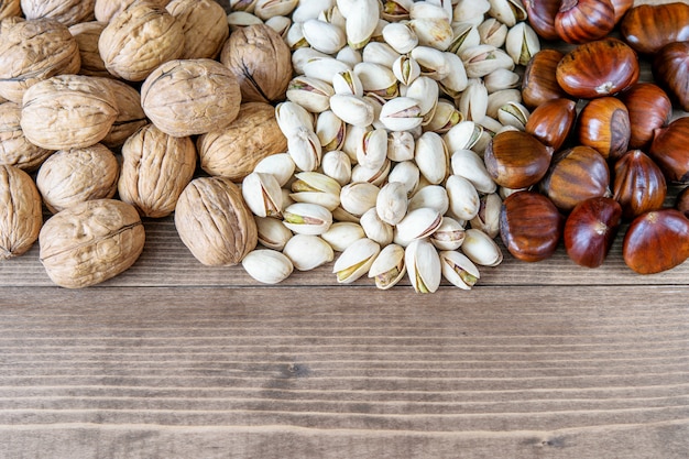 Assortimento di noci, pistacchi e castagne maturi sani freschi maturi sui precedenti di legno