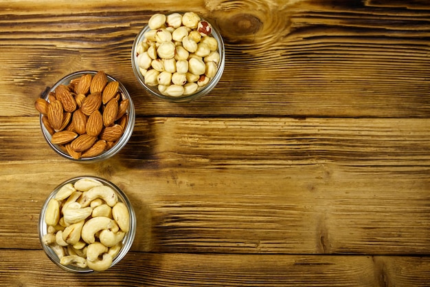 Assortimento di noci su tavola di legno Mandorla nocciola e anacardi in ciotole di vetro Spazio per la copia vista dall'alto Concetto di alimentazione sana