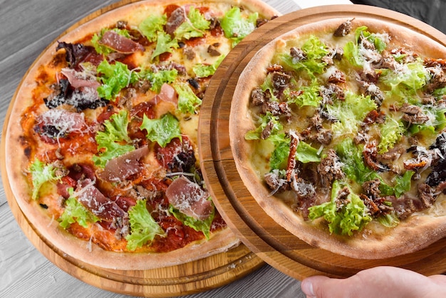 Assortimento di pizze fresche italiane con prosciutto, salame, carne, pomodori, insalata e parmigiano su una tavola di legno su un tavolo di legno.