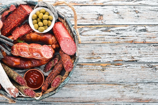 Assortimento di salsicce e snack in una scatola di legno Salsiccia Fuet salame paperoni Su sfondo bianco di legno Vista dall'alto Spazio libero per il testo