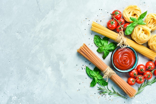 Assortimento di spaghetti colorati secchi e pasta con pomodorini e ingredienti su sfondo di pietra grigia Pasta secca Vista dall'alto Spazio libero per il testo