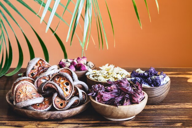 Assortimento di tè tropicale sano a base di erbe secco in ciotole di legno e foglia di palma su fondo rustico.