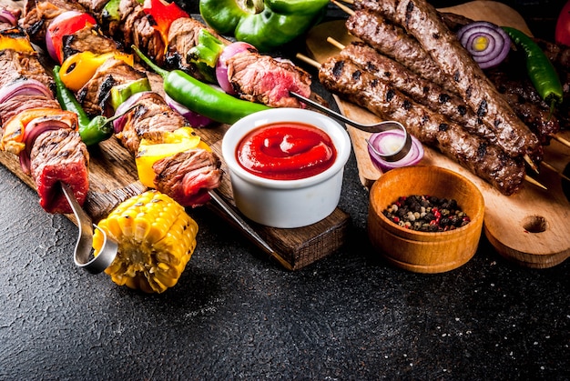 Assortimento di vari barbecue per grigliate di carne, barbecue party fest - shish kebab, salsicce, filetto di carne alla griglia, verdure fresche, salse, spezie, tavolo di cemento arrugginito scuro, sopra lo spazio della copia