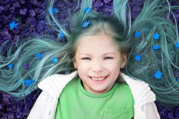 Astratto colorato di bella bambina sorridente sdraiata sul prato fiorito in primavera e guardando la fotocamera.