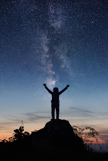 Astronauta in piedi in cima alla montagna sotto il cielo notturno