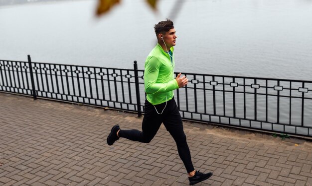 Athelte uomo che corre al mattino sullo sfondo del lago di nebbia Runner maschio che fa jogging nel parco e ascolta la musica sugli auricolari Concetto di persone e sport