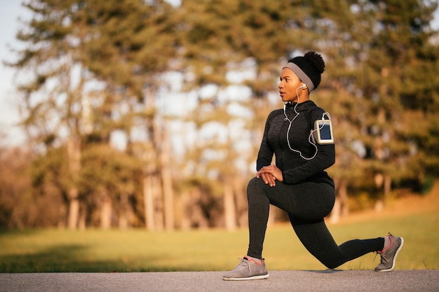 Atleta afroamericana che fa esercizi di stretching mentre si riscalda in natura Spazio di copia