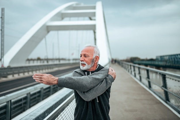 Atleta anziano che si estende sul ponte in città.