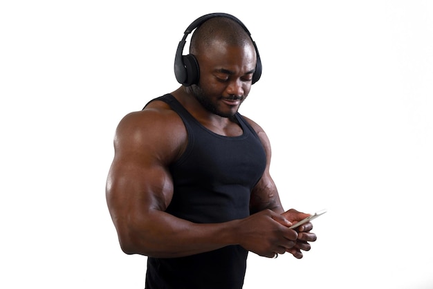 Atleta bodybuilder con bel busto isolato su sfondo bianco Uomo africano che ascolta la musica utilizzando le cuffie wireless