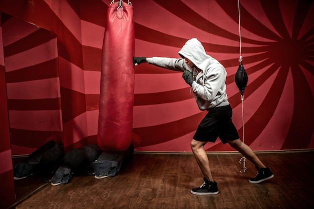 Atleta con felpa con cappuccio che si allena in palestra di boxe preparandosi per la lotta