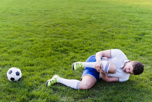 Atleta con gamba ferita sdraiato sull&#39;erba