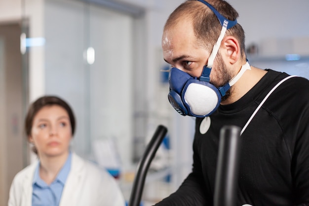 Atleta corridore che testa la frequenza cardiaca cardio nel laboratorio di resistenza sportiva con maschera ed elettrodi sul corpo, vo2. Allenamento sportivo con sensore sulla ricerca incrociata.