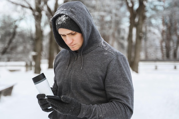 Atleta del giovane che utilizza smartphone durante l'allenamento invernale nel parco cittadino innevato