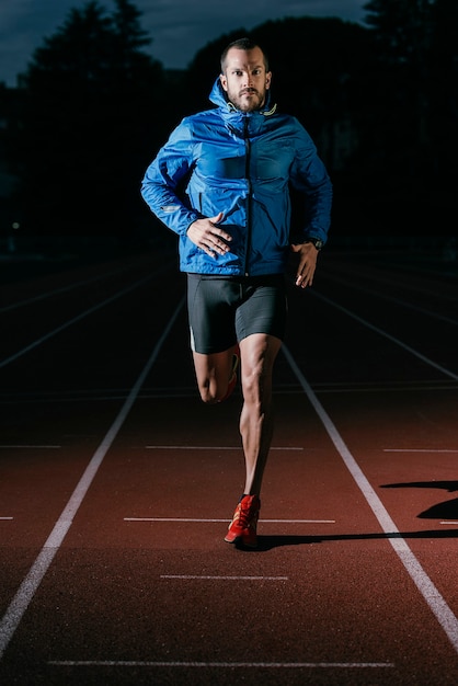 Atleta di pista uomo attraente che corre in pista guardando la telecamera