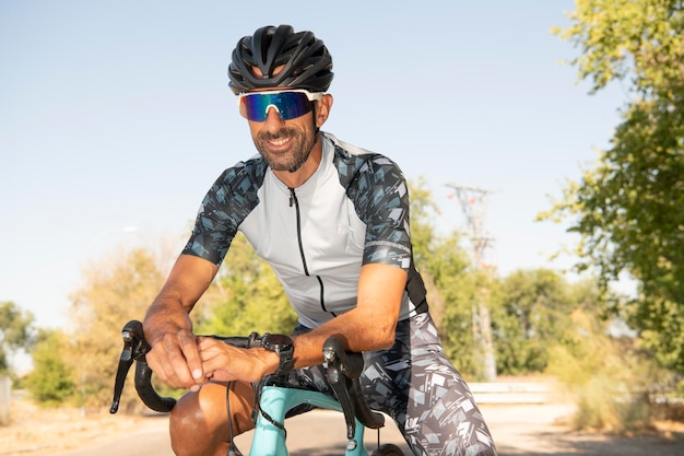 Atleta di triathlon appoggiato al manubrio sorridente con casco e occhiali da sole. Sicurezza