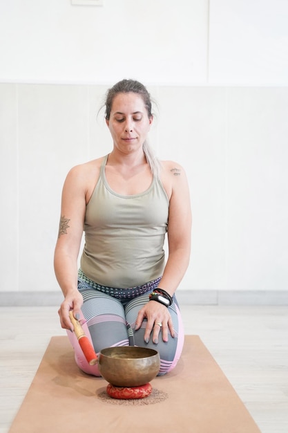 Atleta donna in posizione yoga Virasana o posa dell'eroe che suona una ciotola tibetana