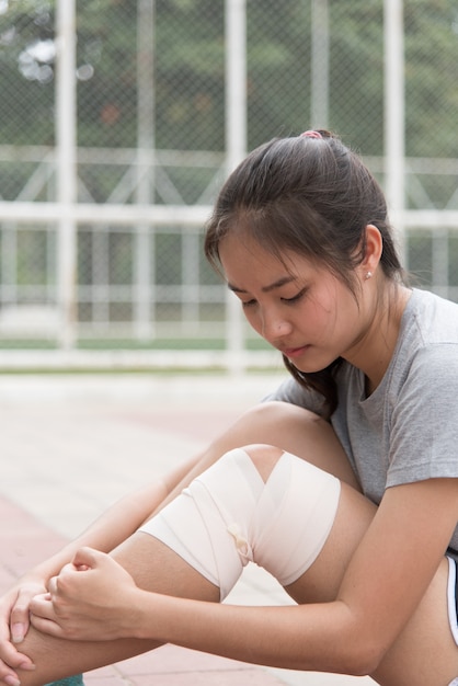 Atleta femminile asiatico che si siede accanto allo stadio Ha avuto un infortunio al ginocchio e ha ottenuto il suo primo soccorso.