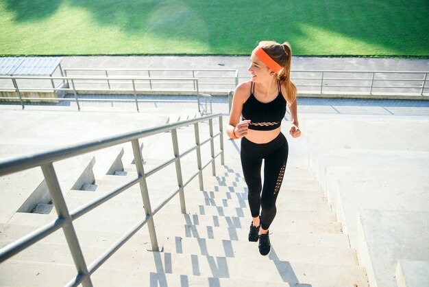 Atleta femminile che corre su per le scale di uno stadio. Donna in abbigliamento fitness facendo allenamento in esecuzione sulle scale accanto ai sedili di uno stadio.