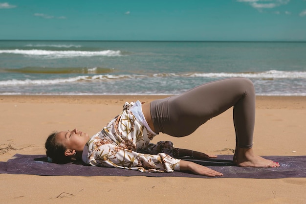 Atleta femminile che esegue esercizio di pilates sulla spiaggia