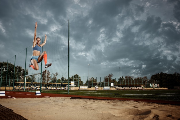 Atleta femminile che salta all'allenamento allo stadio. Il concetto di salto, atleta, azione, movimento, sport, successo e allenamento