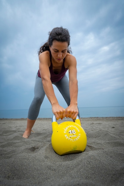 Atleta femminile che si esercita in spiaggia con le campane del bollitore