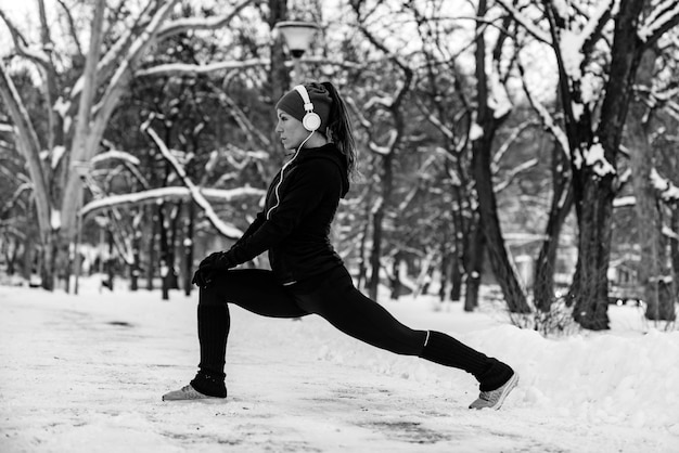 Atleta femminile che si esercita nel parco in una giornata invernale Ascolto di musica ed esercizio fisico