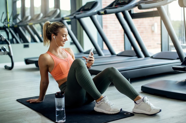 Atleta femminile felice che utilizza il telefono cellulare mentre si prende una pausa dall'esercizio in palestra