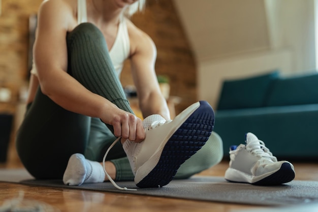 Atleta femminile irriconoscibile seduto sul pavimento e indossare scarpe sportive