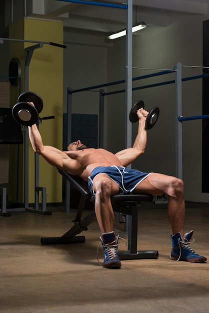 Atleta in forma che allena i curl di concentrazione con manubri pettorali