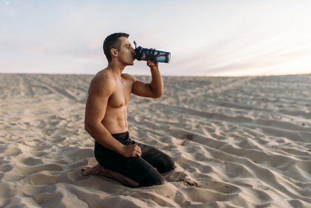 Atleta maschio beve l'acqua dopo l'allenamento nel deserto