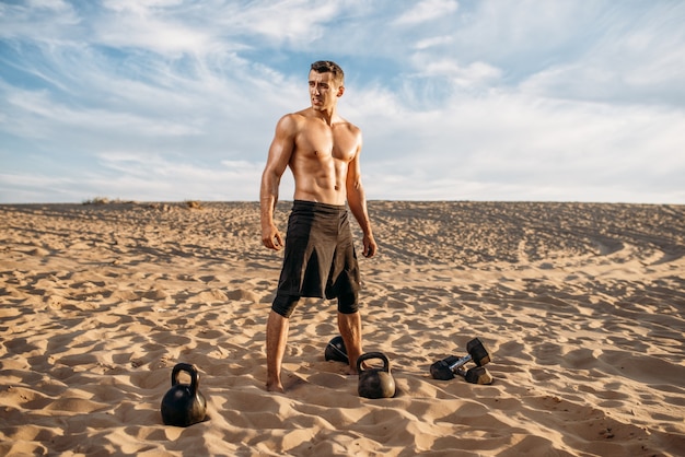 Atleta maschio che fa esercizi con manubri nel deserto alla giornata di sole. Forte motivazione nello sport, allenamento di forza all'aperto