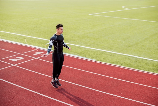 Atleta maschio che salta sulla pista di corsa rossa nello stadio