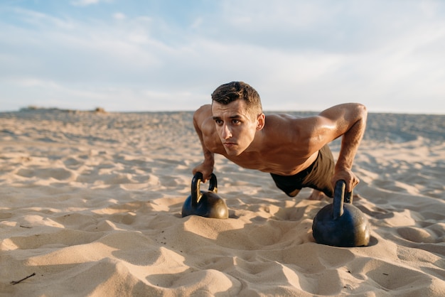 Atleta maschio facendo esercizi push-up con due kettlebell nel deserto al giorno pieno di sole. Forte motivazione nello sport, allenamento di forza all'aperto