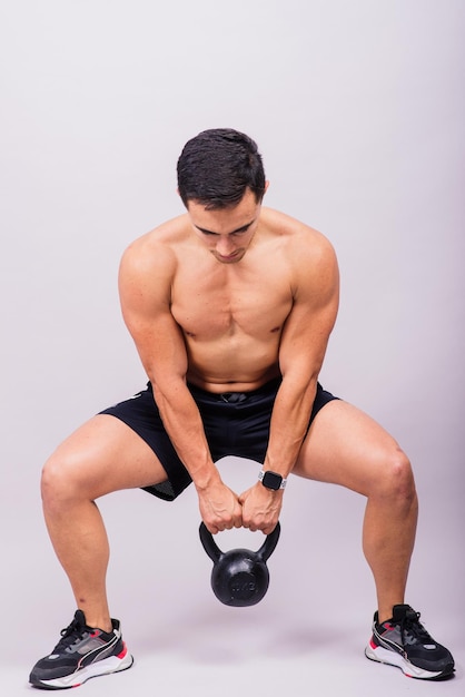 Atleta maschio ispanico che lavora con kettlebell su sfondo grigio tema di allenamento crossfit